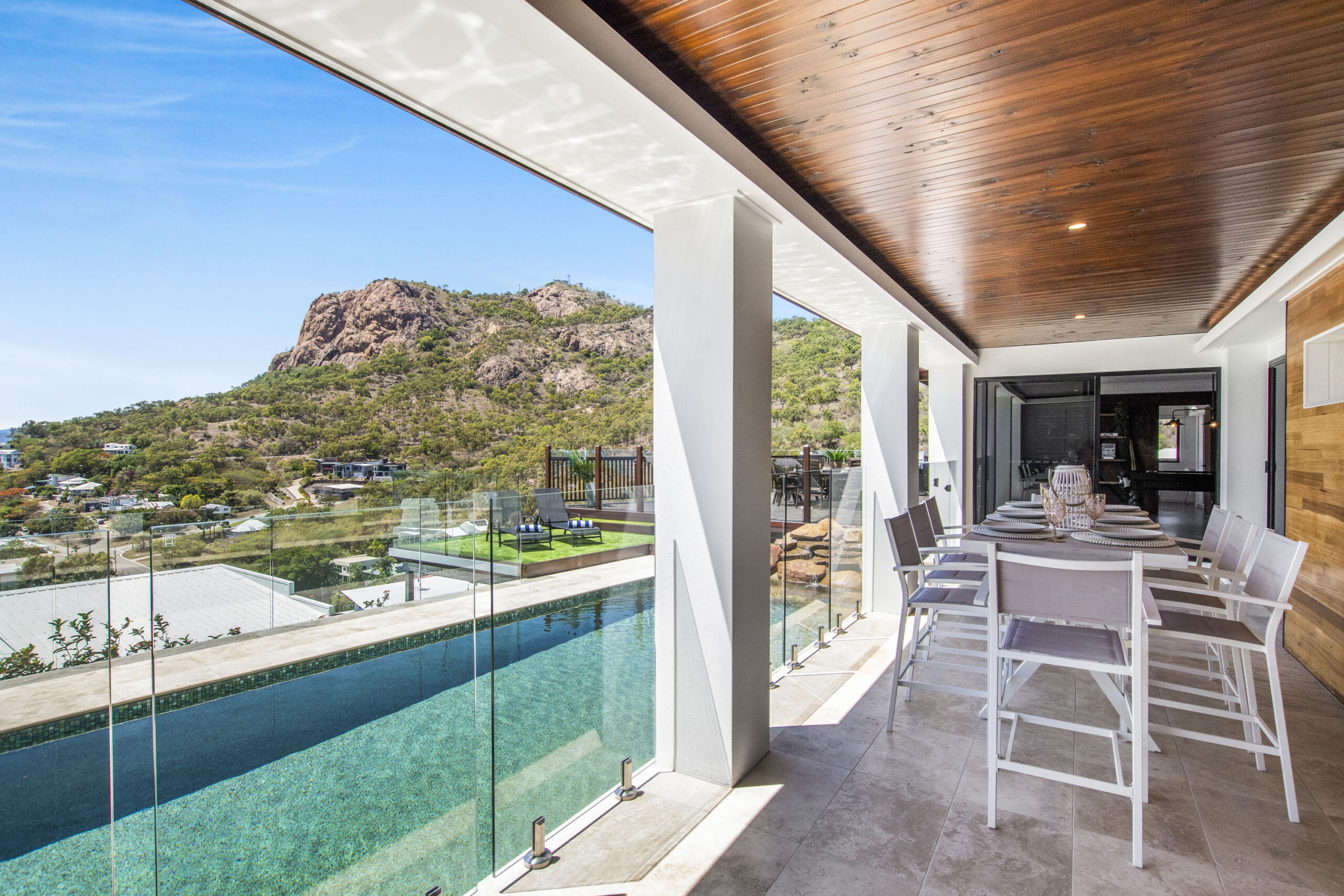 A deck view from premium accomodation shows an infinity pool with blue sky views of Townsville's iconic Castle Hill.